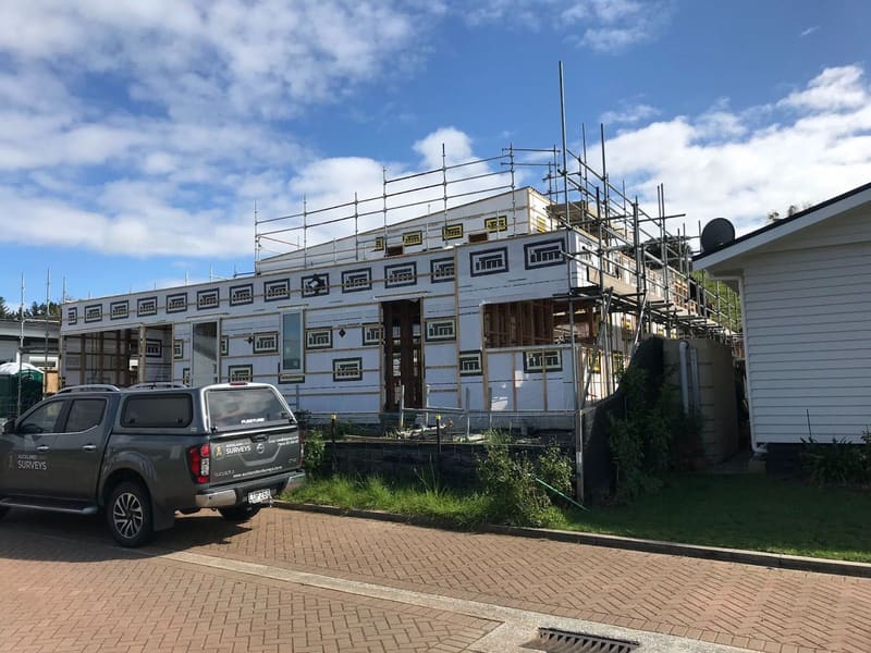 Auckland Land Surveys vehicle parked beside a house under construction with scaffolding and building wrap