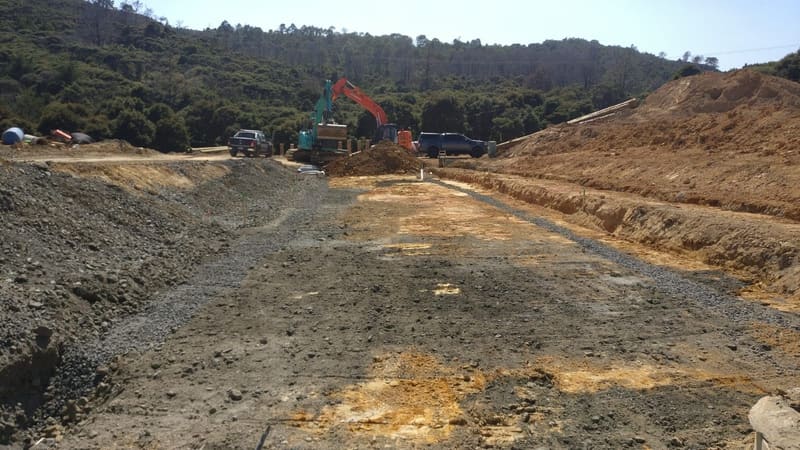 Land development site under earthworks with excavators working beside regenerating bush